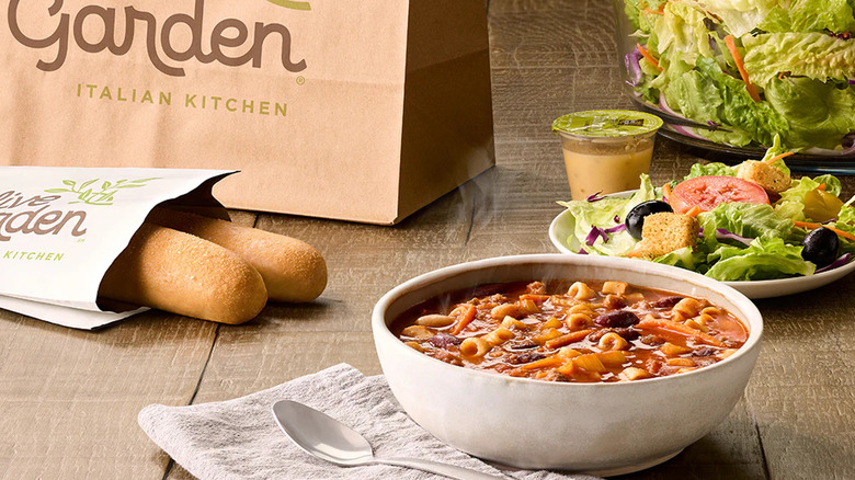 Olive Garden lunch special with soup, salad, breadsticks, and paper bag on table