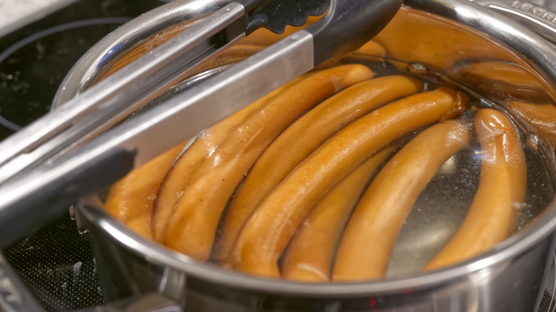 tongs resting on pot filled with cooking hot dogs