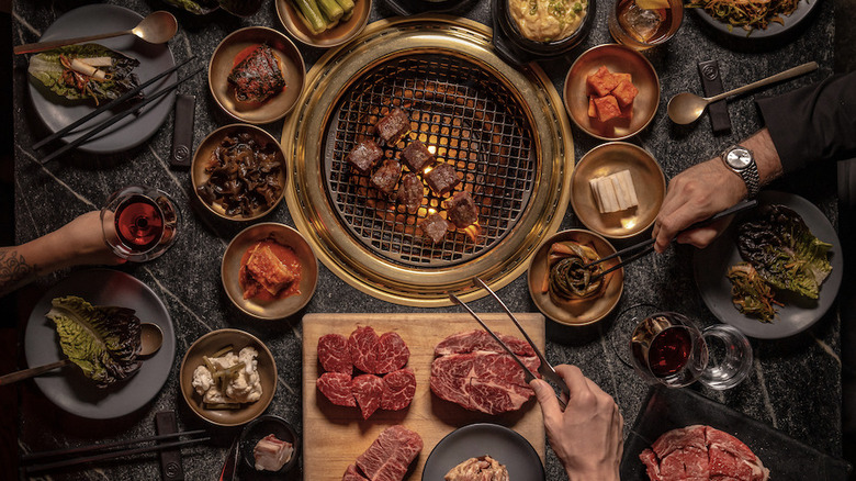 A lush table full of meat and other raw foods with a Korean style grill in the middle