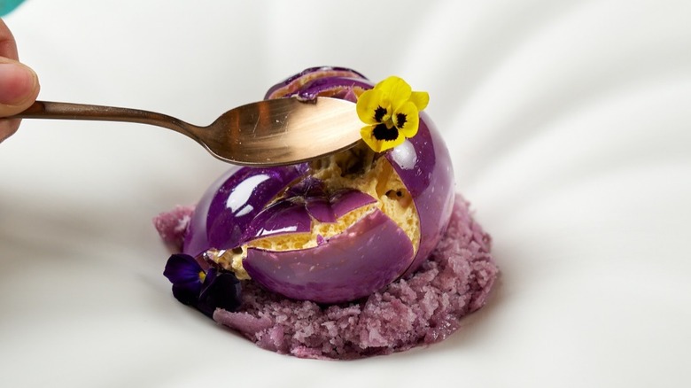 A spoon cracking the shell on a purple dessert