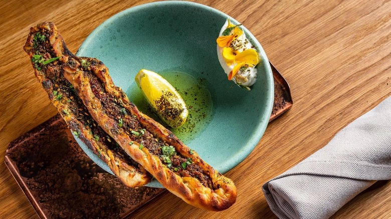 Sfeeha balanced on a blue plate with lemon and olive oil, flower garnish