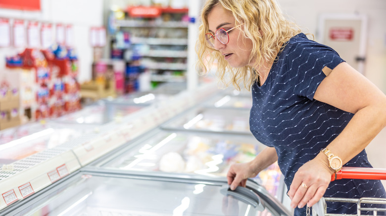 woman peering into freezer case in store