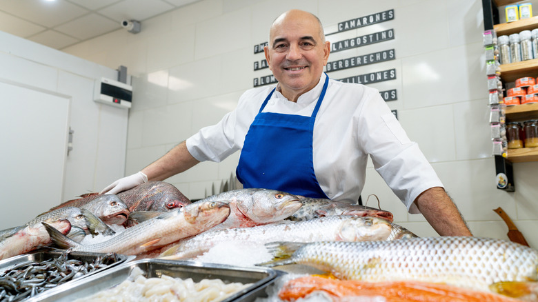 man in apron standing behind fish counter