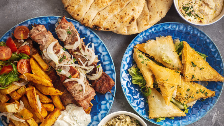 Plates of souvlaki, fries, spanakopita, hummus, and pitas