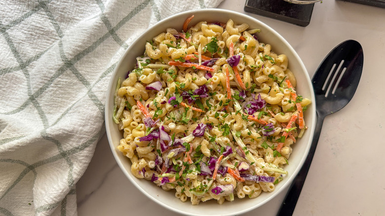 A white bowl of macaroni salad next to a black serving spoon
