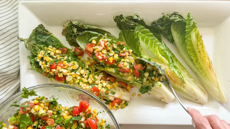 Someone spooning corn relish onto romaine leaves on a white rectangular plate