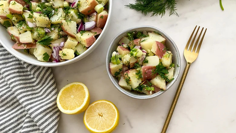 Small and large bowls of herbed potato salad next to a halved lemon and a fork