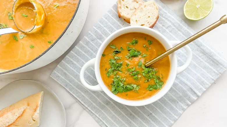 A white crock of simple roasted butternut squash soup garnished with parsley sprigs