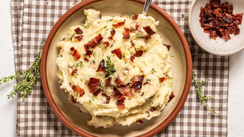 A rustic brown bowl of bacony mashed potatoes garnished with thyme