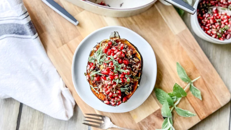A white plate of wild rice and walnut-stuffed acorn squash on a wooden cutting board