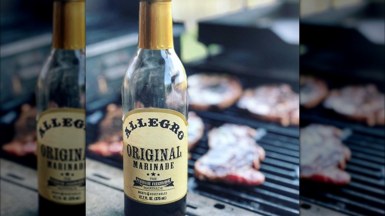 A bottle of Allegro marinade in front of a grill with steaks