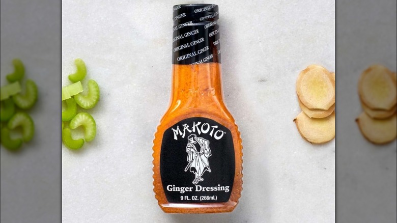 A bottle of Makoto ginger dressing on a white countertop with ginger and celery