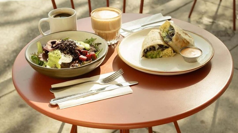 Two lunch dishes with cutlery and two coffees on small round outdoor table