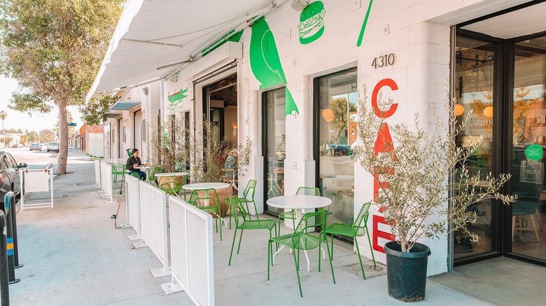 The outdoor patio with green chairs, white, tables, and an orange sign at Highly Likely cafe