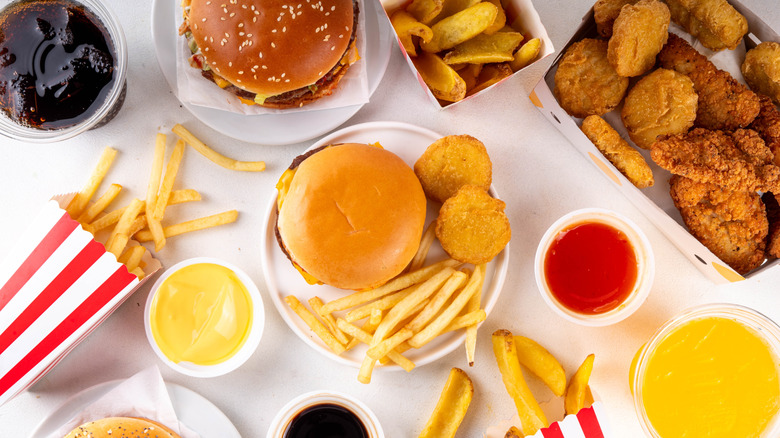 Flatlay of fast food items including french fries, soda, hamburgers, cheese sauce, and chicken nuggets
