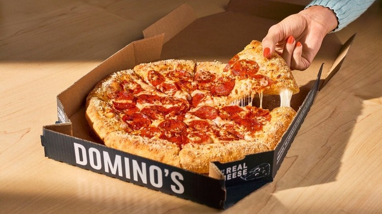 Person grabbing a cheesy slide of Parmesan stuffed crust pepperoni pizza from Domino's