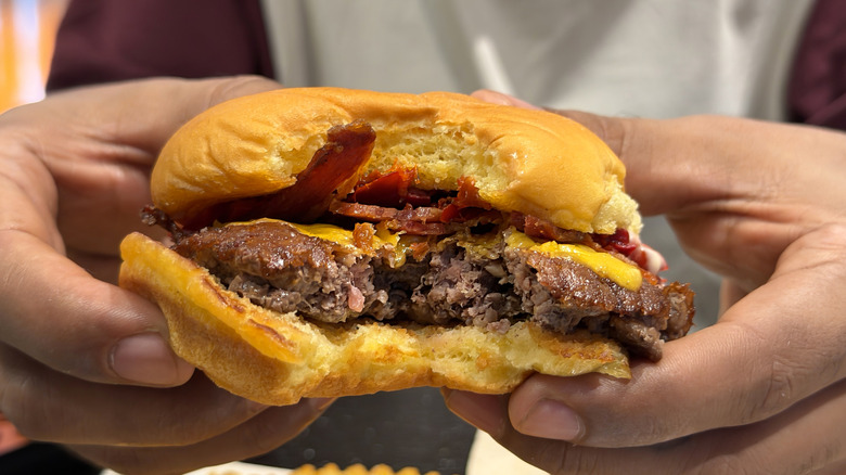 Close-up of hands holding a smashburger with a bite taken out of it.