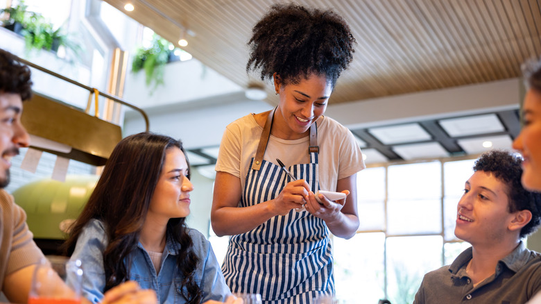 Waitress wearing a striped apron taking an order on a notepad