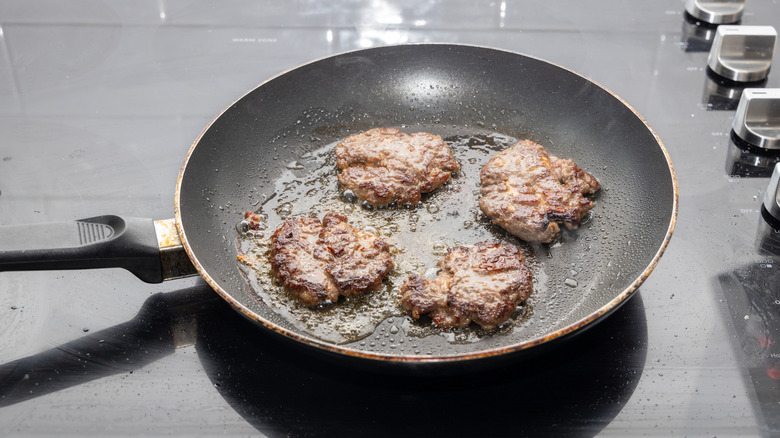Four sliders cook in a pan on the stove.
