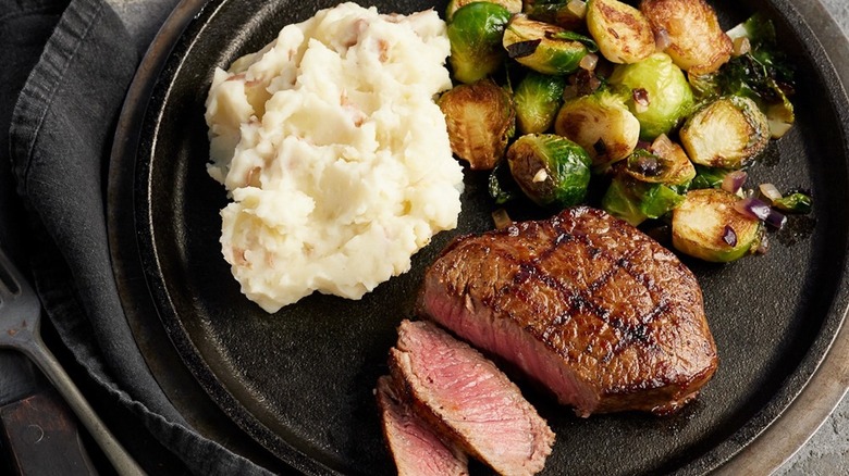 Steak, Brussels sprouts, and mashed potatoes on a black plate at Black Angus Steakhouse