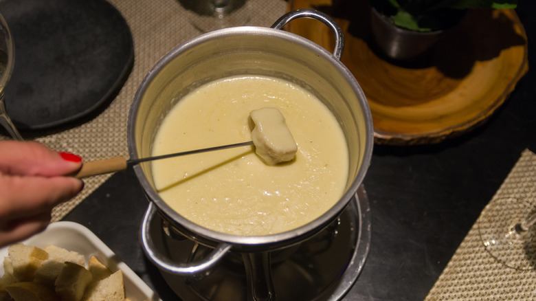 Hand dipping bread into cheese fondue