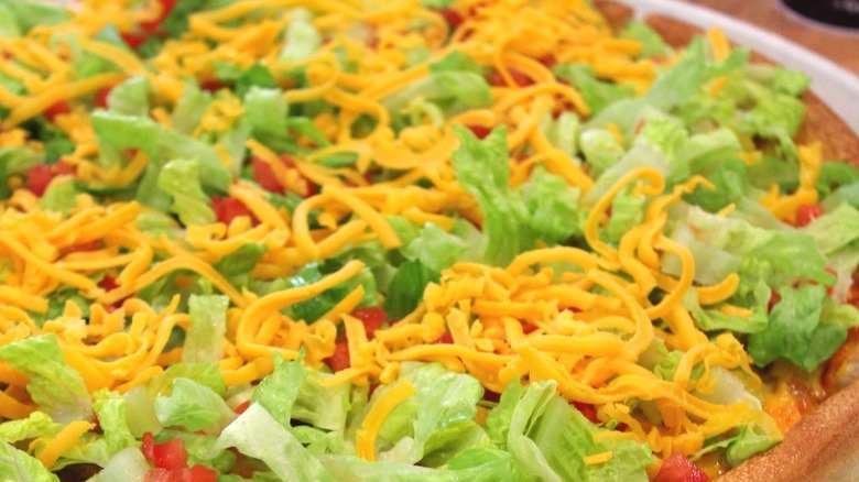 A close up of the taco pizza from Godfather's Pizza, highlighting its shredded cheese and lettuce.