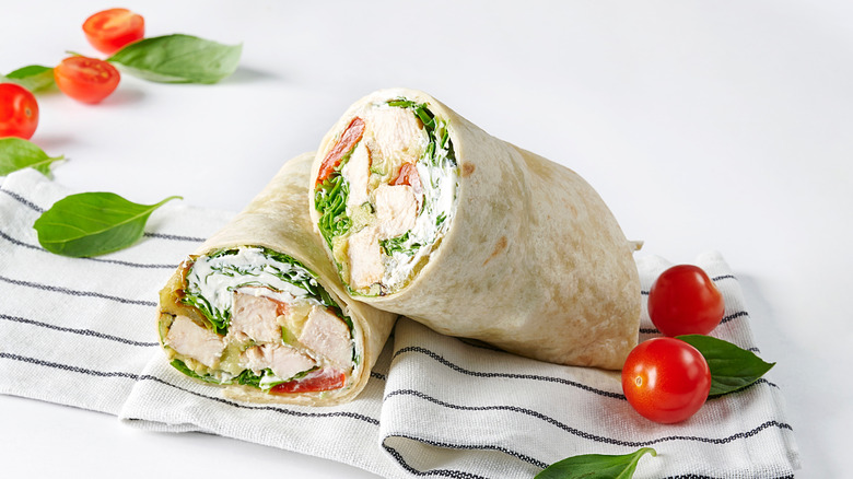 Chicken Caesar salad wrap with sliced tomatoes and basil leaves