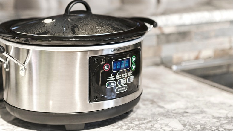 Black and silver slow cooker set to low on top of a grey kitchen counter