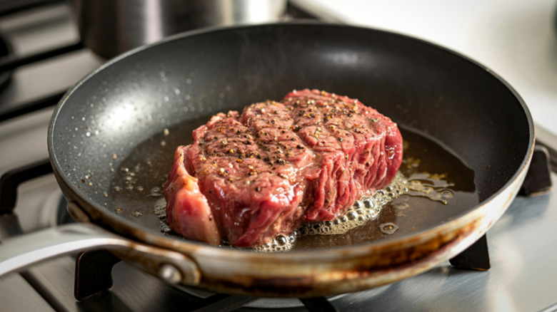 Raw steak searing in pan with oil
