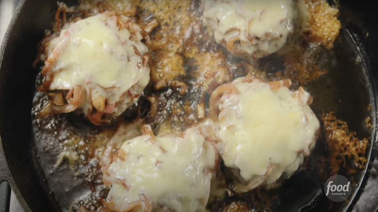 Ina Garten's caramelized onion and Gruyère smash burgers cooking in a cast iron pan
