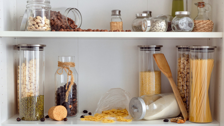 A cluttered kitchen cabinet with containers of ingredients, some of them spilling out, creating unsightly mess.