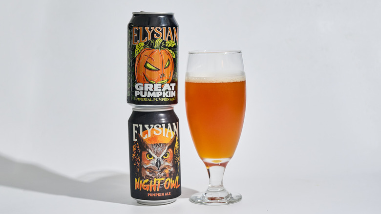 Cans of Elysian Night Owl and Great Pumpkin Imperial Ale stacked on a table next to a glass of beer.