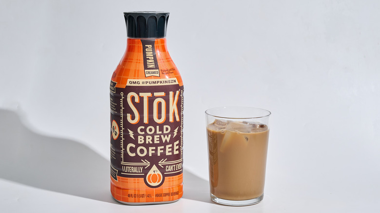 A bottle of Stok Pumpkin Cream Cold Brew Coffee on a table with a glass of cold brew.