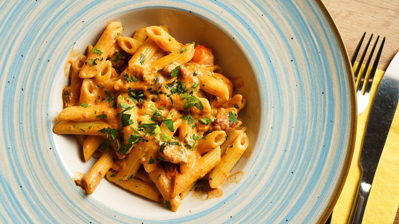 Creamy tomato penne pasta with sausage in a blue and white painted bowl.