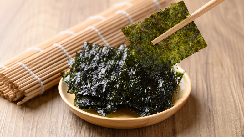 chopsticks picking up nori besides sushi mat