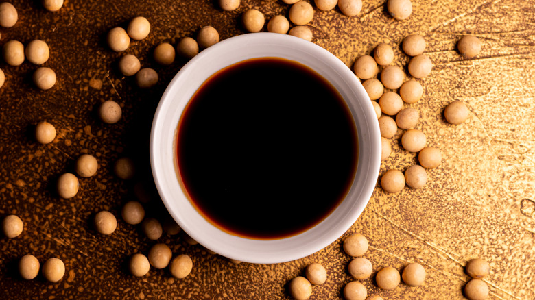 dish of soy sauce surrounded by scattered soybeans