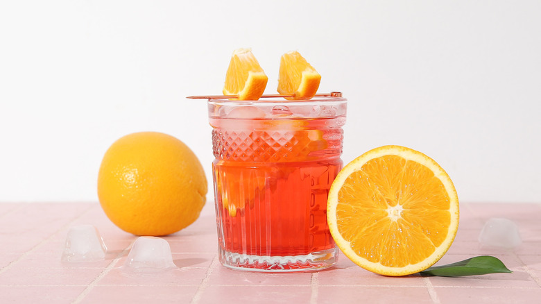 A pink-ish drink is arranged with oranges on a bright, white and light pink background.