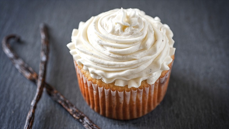 One vanilla cupcake with piped white frosting over a gray background