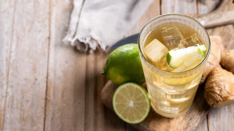 A light, iced drink in a glass is pictured from above with ginger and limes in the frame.