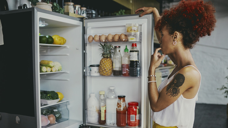 A person is seen peering into an open refrigerator.