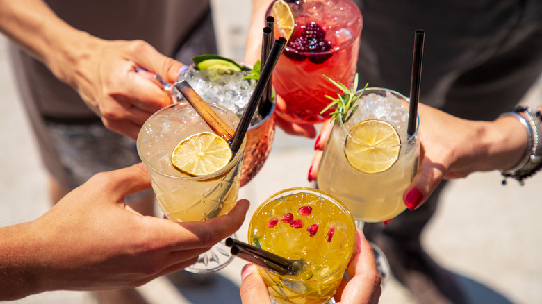 Hands hold five different vibrant cocktails