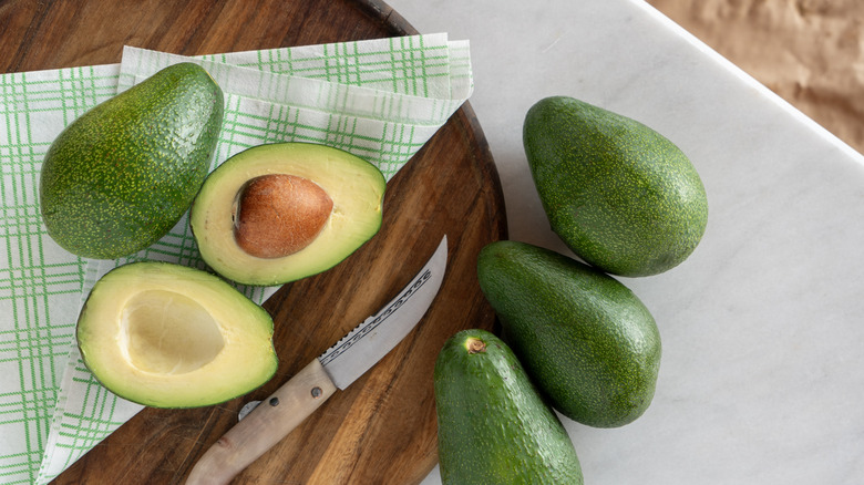 whole and sliced avocados on a wooden cutting board