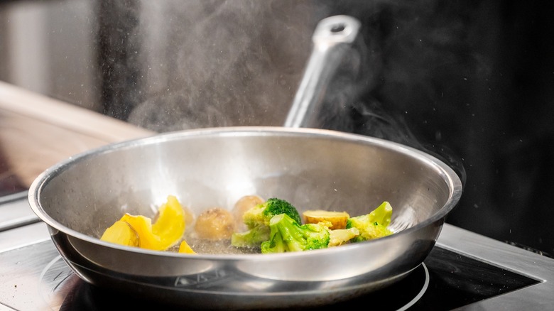 stainless steel pan with vegetables sizzling on stove