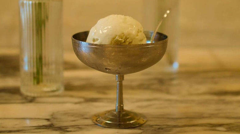 A scoop of light-colored ice cream in a stemmed silver dish.