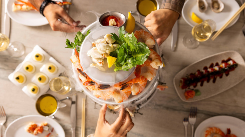 People's hands are seen reaching for items on a seafood tower in an overhead photo.