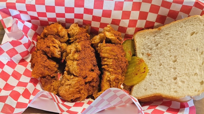 Three chicken tenders with pickles and a slice of bread in checkered red and white paper