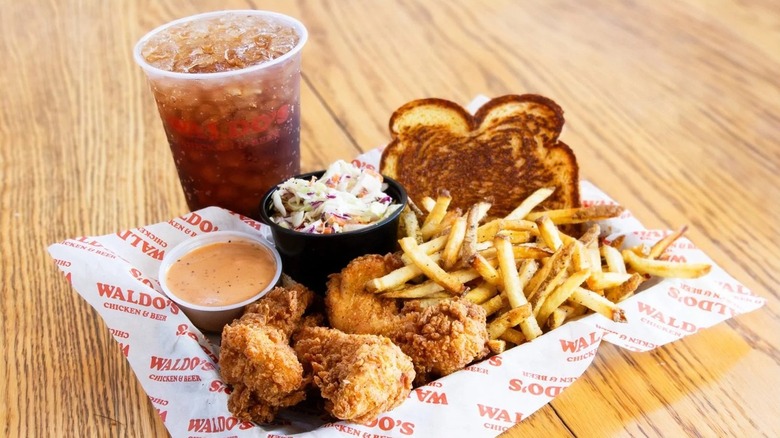 A plate of chicken tenders with fries, coleslaw, bread, and a soda