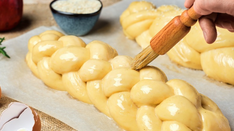 Braided challah loaves get egg wash for that characteristic shine and color