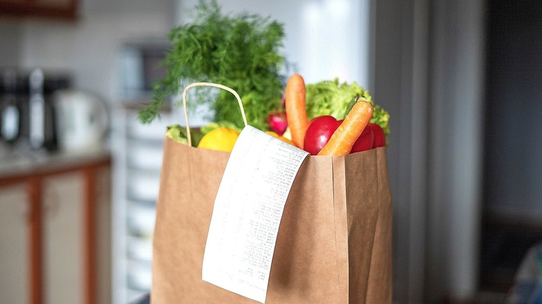 Brown bag full of fresh fruit vegetables and long grocery receipt on kitchen counter