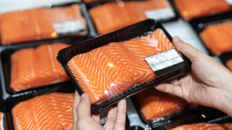 A person grabbing a package of salmon at a grocery store